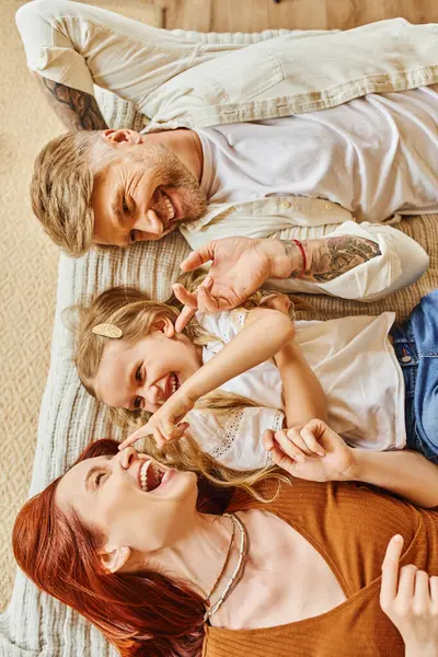 Draufsicht auf freudige Eltern mit niedlicher Tochter, die sich hinlegt und Spaß im Bett hat, Erholungszeit — Stockfoto