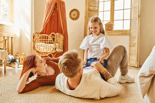 Mulher sorrindo olhando para o marido brincando com a filha no chão na sala de estar, momentos de ligação — Fotografia de Stock