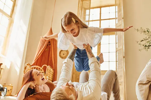 Lachende Frau schaut Ehemann an, der mit Tochter auf dem Fußboden im Wohnzimmer spielt, fesselnde Momente — Stockfoto