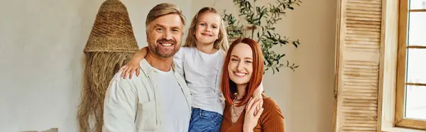 Smiling husband and wife holding cute daughter and looking at camera in cozy bedroom, banner — Stock Photo