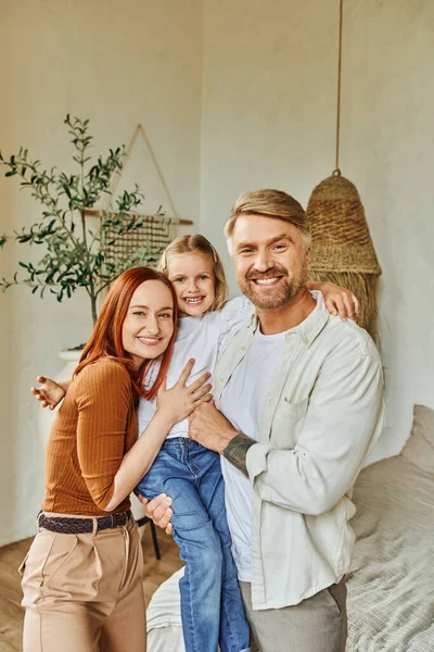 Cheerful husband and wife holding and embracing daughter in bedroom at home, bonding moments — Stock Photo