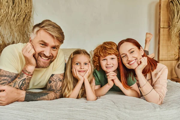 Lächelnde Eltern und glückliche Kinder, die zu Hause auf dem Bett liegen und in die Kamera schauen, Erholungszeit — Stockfoto