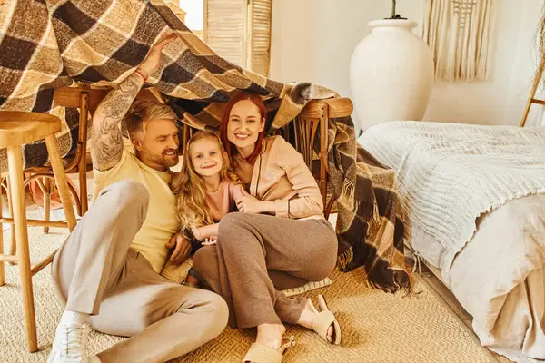 Веселые родители с счастливой дочерью прячутся под одеялом хижина в гостиной, играть вместе — стоковое фото