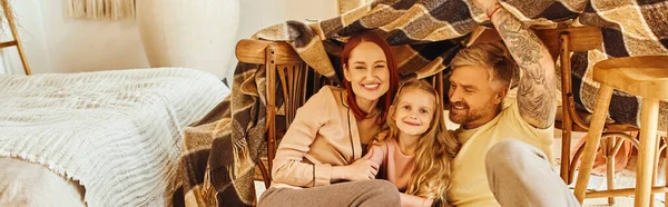 Joyful parents with happy daughter playing under blanket hut in living room, horizontal banner — Stock Photo