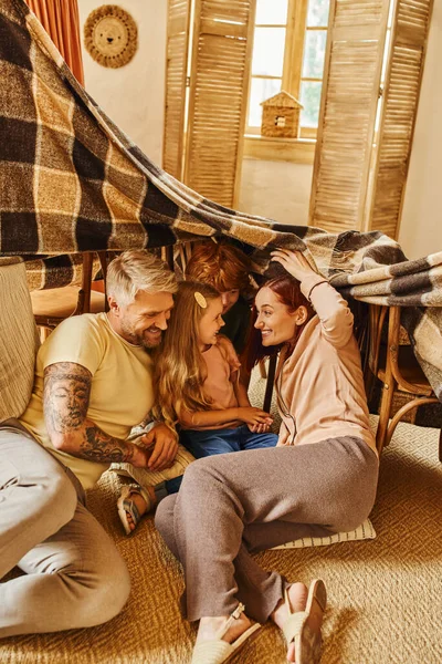 Happy children with parents playing under blanket hut in living room at home, emotional connection — Stock Photo