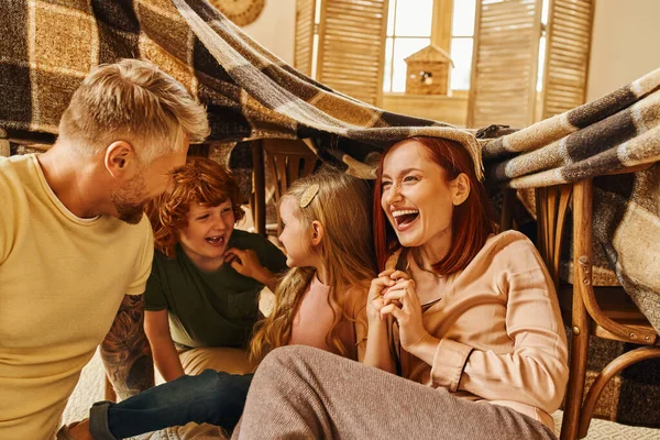 Genitori felicissimi che ridono sotto la coperta mentre giocano con i bambini in soggiorno, momenti di legame — Foto stock