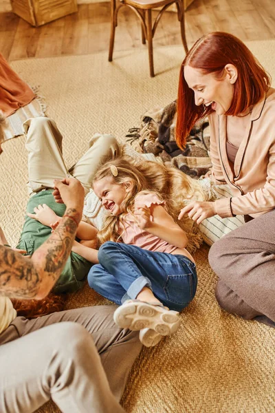 Pais alegres brincando com crianças despreocupadas no chão na acolhedora sala de estar em casa, momentos alegres — Fotografia de Stock