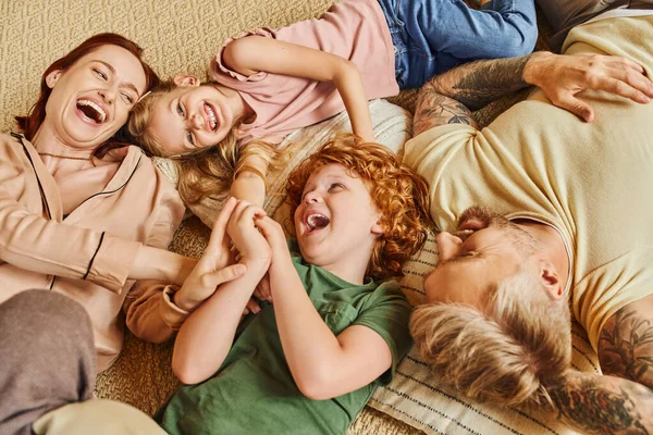 Vista dall'alto di genitori gioiosi e bambini sdraiati e sul pavimento in un moderno soggiorno, divertimento e risate — Foto stock