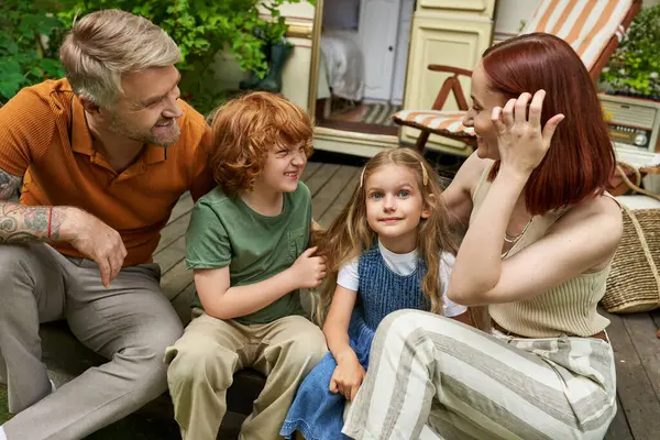 Smiling parents talking to daughter and son while sitting near trailer home, bonding moments — Stock Photo