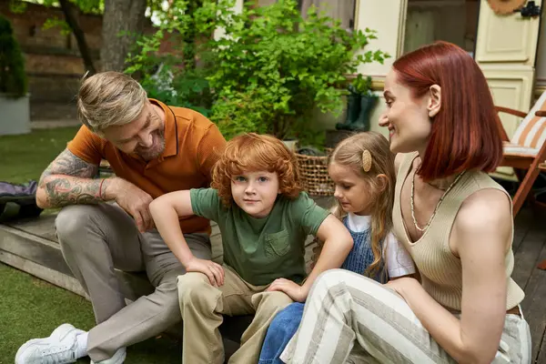 Carino rossa ragazzo guardando fotocamera mentre seduto con felice famiglia vicino rimorchio casa, tempo libero — Foto stock