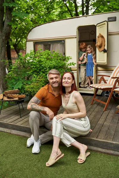 Радісний чоловік і дружина сидять і дивляться на камеру біля дітей в трейлері будинку, сімейне дозвілля — стокове фото