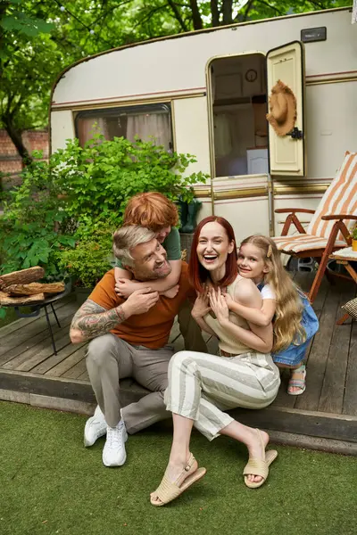 Bambini eccitati che abbracciano i genitori ridenti seduti a casa roulotte all'aperto, momenti di legame — Foto stock