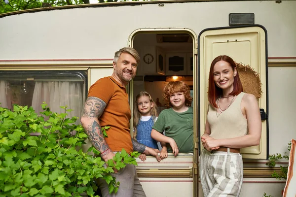 Smiling parents looking at camera near happy children in trailer home, family leisure and recreation — Stock Photo