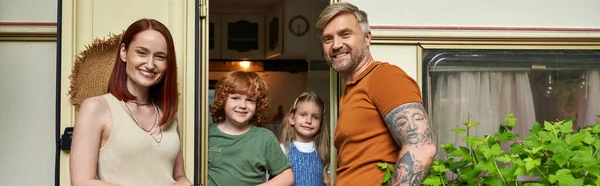 Joyful couple looking at camera near happy children in trailer home, family leisure, banner — Stock Photo