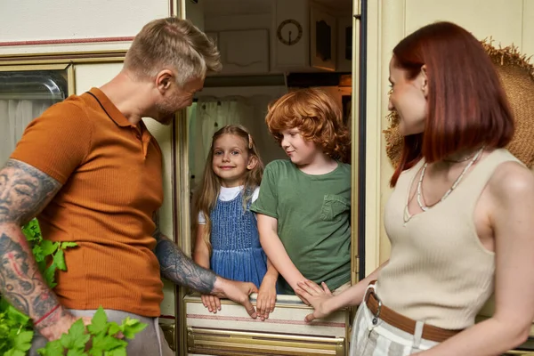 Padres felices mirando a la hija y el hijo divirtiéndose en casa remolque, ocio familiar y recreación - foto de stock