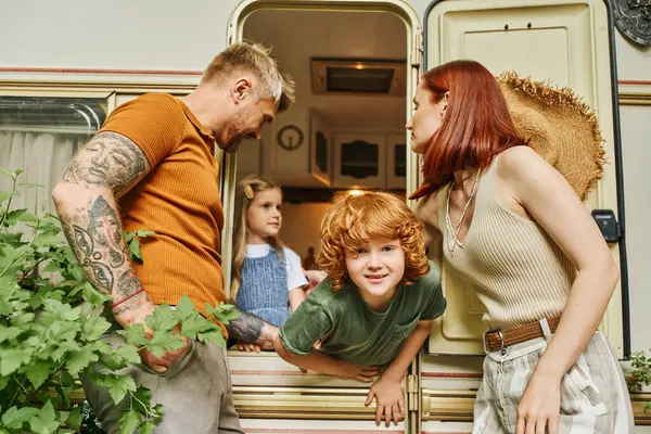 Happy couple looking at camera near kids having fun in trailer home, family leisure and recreation — Stock Photo