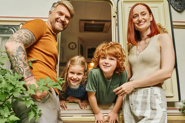 Joyful couple looking at camera near kids having fun in trailer home, family leisure and recreation — Stock Photo