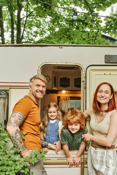 Fröhliches Paar lächelt in die Kamera in der Nähe von Kindern, die Spaß im Wohnwagen haben, Familienzeit — Stockfoto