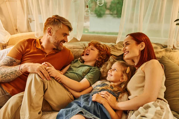 Joyful couple with excited kids relaxing and having fun on soft bed in cozy trailer home, leisure — Stock Photo