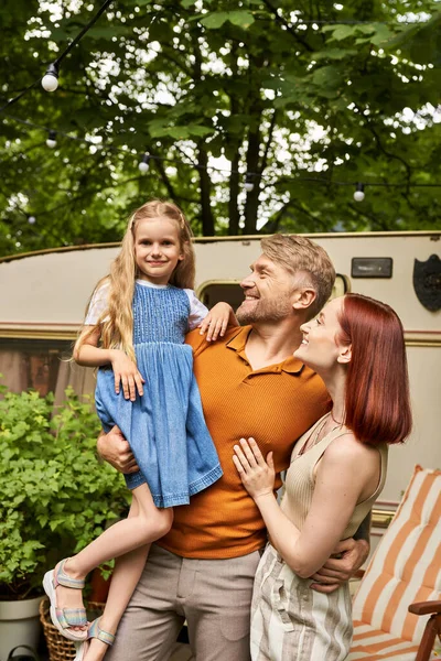Sorridente homem segurando bonito filha perto feliz esposa e reboque casa no parque, família ligação — Fotografia de Stock
