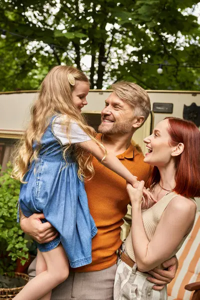 Счастливый мужчина, держащий восхитительную дочь рядом с улыбающейся женой и современным домом, отдых и приключения — стоковое фото