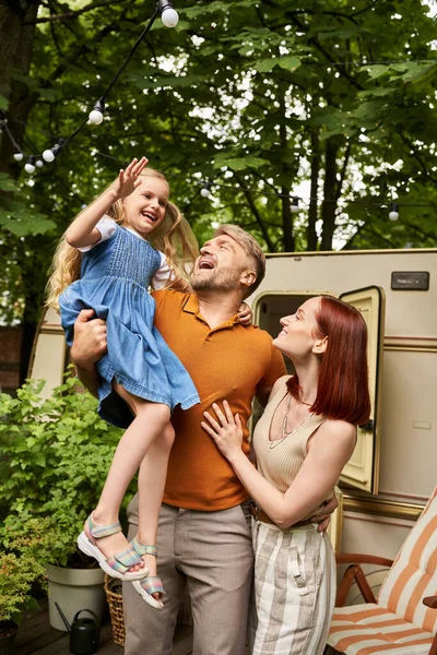 Aufgeregter Mann mit glücklicher Tochter neben lächelnder Frau und modernem Wohnwagen nach Hause, Freizeit und Abenteuer — Stockfoto