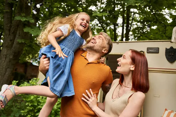 Отец держит сверх радостной дочери рядом улыбается жена и современный трейлер домой, весело и смех — стоковое фото