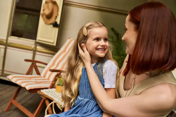 Happy woman stroking hair of adorable daughter while sitting next to trailer home, love and care — Stock Photo