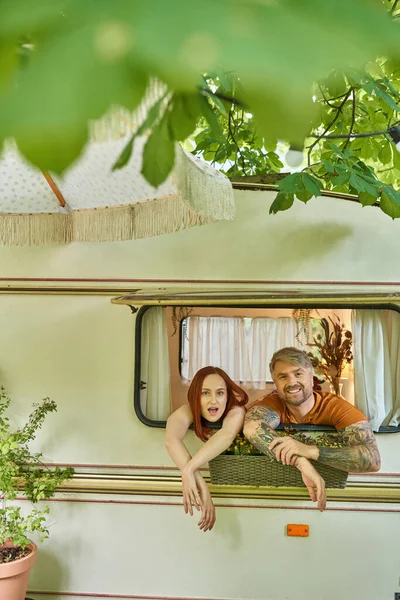 Excité rousse femme et sourire tatoué homme dans la fenêtre de la maison remorque moderne, loisirs en famille — Photo de stock