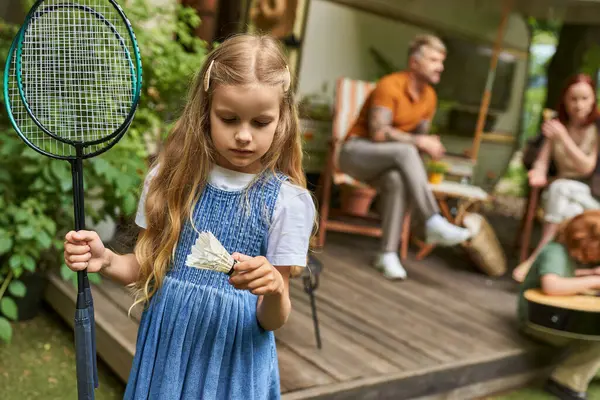 Fille tenant roquettes de badminton et navette près de la famille et la maison de remorque sur fond flou — Photo de stock