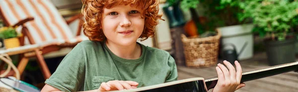 Redhead kid with acoustic guitar looking at camera while sitting near modern trailer home, banner — Stock Photo