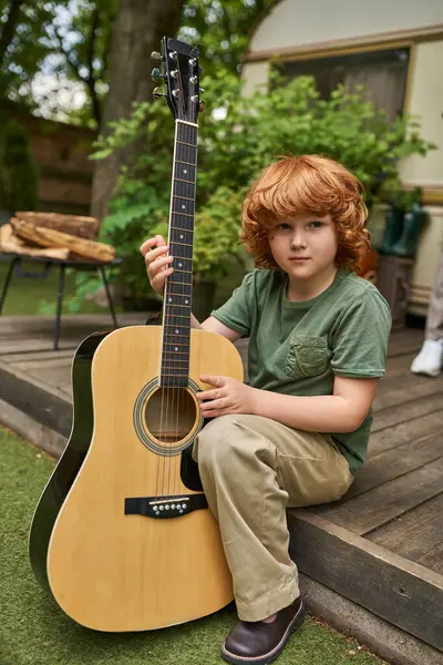 Confident redhead boy with acoustic guitar looking at camera while sitting near modern trailer home — Stock Photo