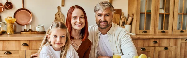 Lächelnde Eltern mit entzückender Tochter, die in der heimischen Küche in die Kamera lächelt, horizontales Banner — Stockfoto