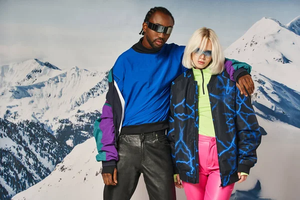 Jovem casal interracial abraçando e olhando para a câmera com pano de fundo de montanha, conceito de inverno — Fotografia de Stock