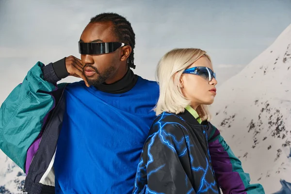 Модная пара в стильных солнцезащитных очках, позируя вместе с горным фоном, зимняя концепция — стоковое фото