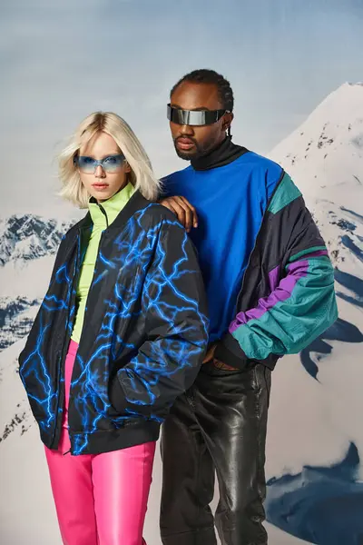 Voguish couple attrayant en tenue vibrante regardant la caméra avec fond neigeux, concept d'hiver — Photo de stock