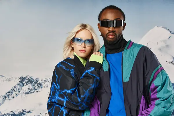 Модная межрасовая пара в яркой одежде в солнечных очках на снежном фоне, зимняя концепция — стоковое фото