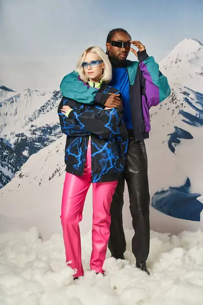 Atraente abraço casal posando em roupas quentes vívidas com óculos de sol elegantes, conceito de inverno — Fotografia de Stock