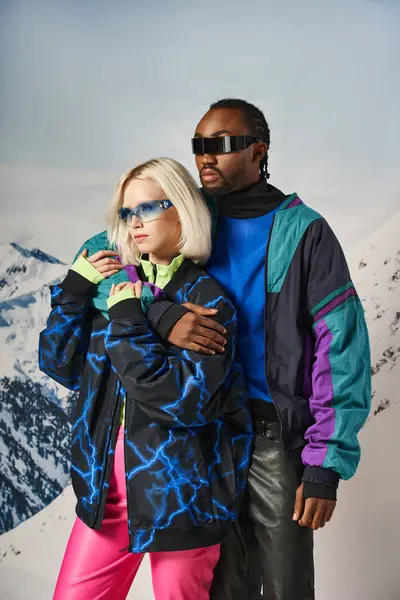 Belo casal multirracial em vibrantes roupas ousadas e óculos de sol elegantes abraçando calorosamente, inverno — Fotografia de Stock