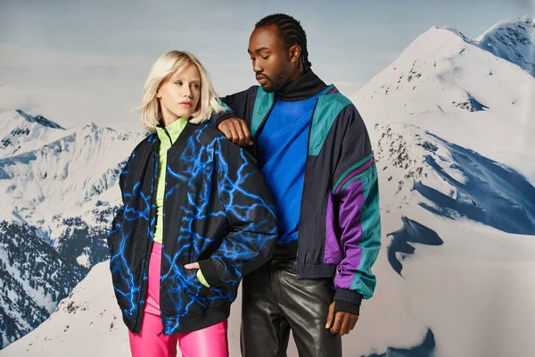 Attrayant couple multiracial en tenues chaudes vibrantes avec la main sur l'épaule, concept d'hiver — Photo de stock