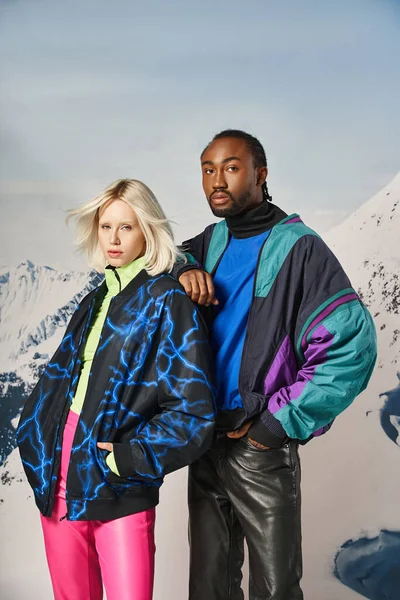 Atractivo joven interracial pareja en caliente elegante atuendo mirando a la cámara, concepto de invierno - foto de stock