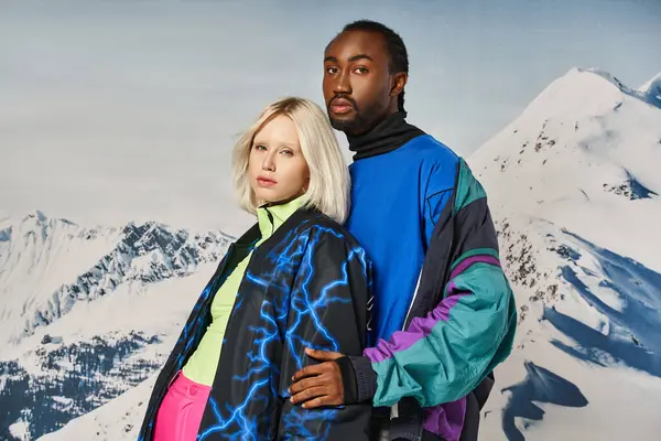 Belo casal diversificado em roupas de inverno na moda abraçando calorosamente e olhando para a câmera — Fotografia de Stock