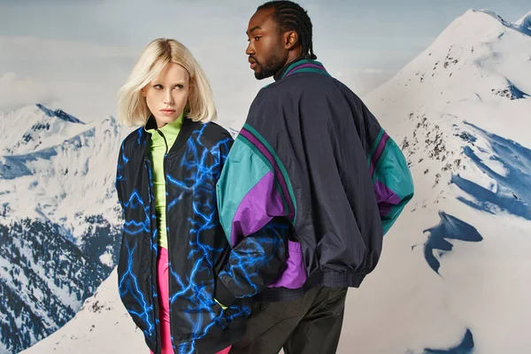 Joven pareja con estilo en ropa de invierno cálido posando junto con fondo de montaña nevada - foto de stock