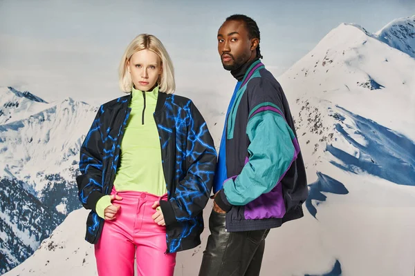 Elegante pareja diversa en traje cálido brillante posando juntos y mirando a la cámara, concepto de invierno - foto de stock