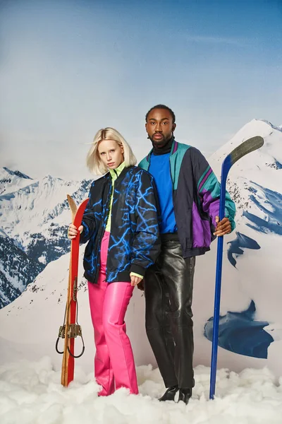 Молодая привлекательная пара в теплых нарядах позирует вместе с лыжами и хоккейной клюшкой, зимняя концепция — стоковое фото