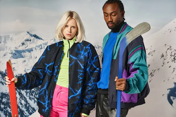 Attractive interracial couple in vibrant warm outfit holding skis and hockey stick, winter concept — Stock Photo