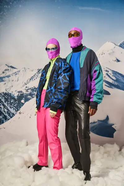 Par multicultural na moda em roupas quentes com balaclavas rosa e óculos de sol, conceito de inverno — Fotografia de Stock