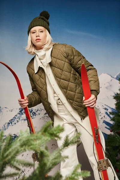 Привлекательная молодая женщина в теплой куртке, позирующая с лыжами на снежном фоне, зимняя концепция — стоковое фото