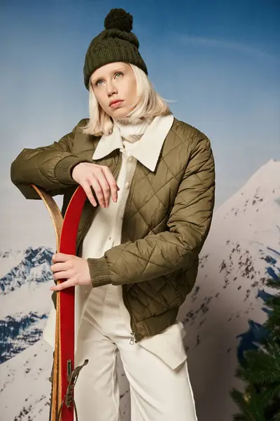 Stylische blonde Frau im Sakko mit Hut und Skiern in den Händen, die wegschauen, Winterkonzept — Stockfoto