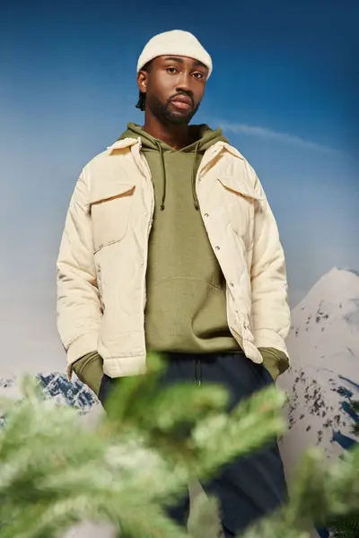 Hombre guapo en gorro sombrero y chaqueta con telón de fondo de montaña mirando a la cámara, concepto de invierno - foto de stock